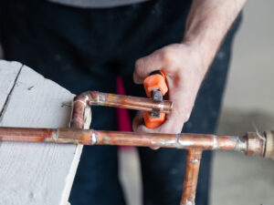 %Focuskw% | Divine Image of a smiling plumber with a clipboard looking under the sink