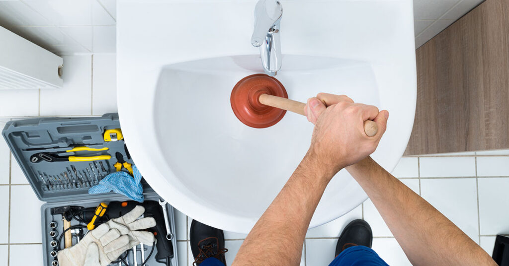 Plumber using a plunger on a sink drain