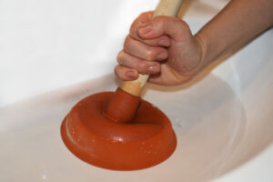 %Focuskw% | Divine Woman with plunger trying to remove clogged sinks.